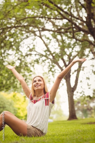 Happy woman with hands raised while sitting on grass 