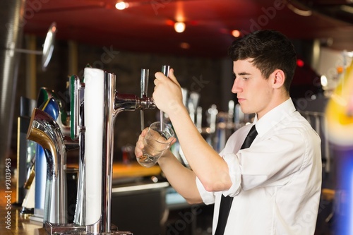 Barkeeper holding glass in front of beer dispenser at bar