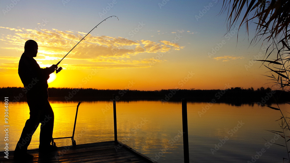 Young man fishing on a lake at sunset Young man fishing on a lake at sunset