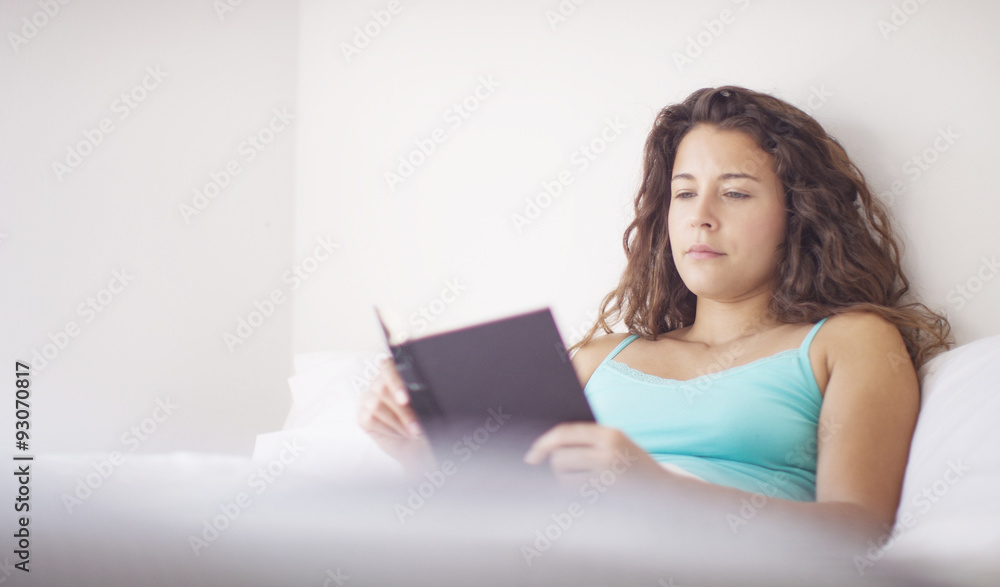 Yong attractive woman reading a book in bed in the morning sunlight Yong attractive woman reading a book in bed in the morning sunlight
