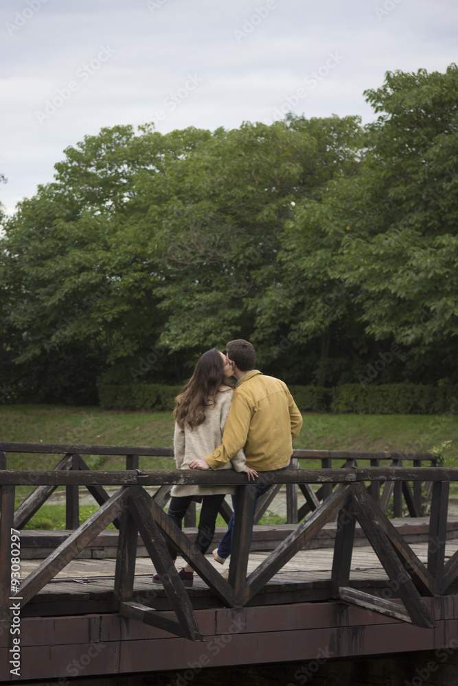 Young couple in 20s, leaning on wooden bridge. In nature, park. Young couple in 20s, leaning on wooden bridge. In nature, park.