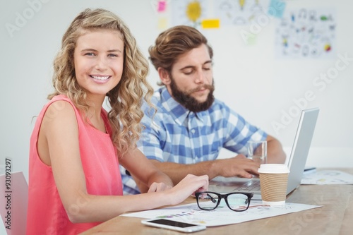 Portrait of smiling woman with man working on laptop 