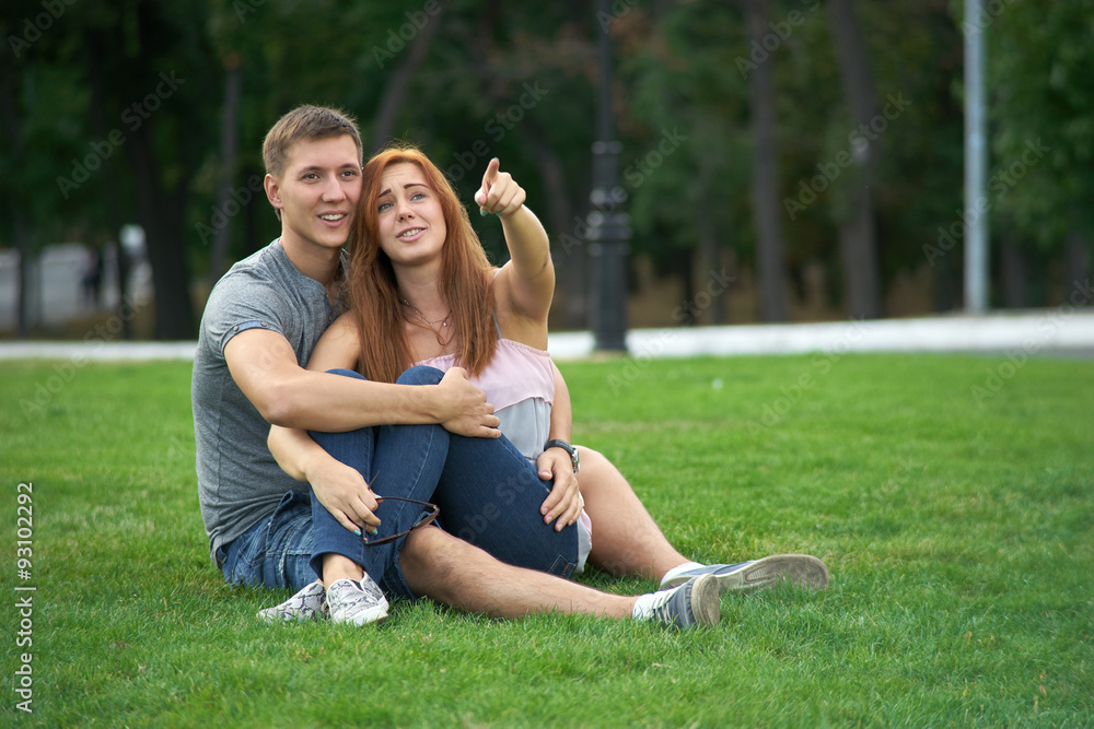 couple sitting on the grass in the park. Woman shows a finger gu