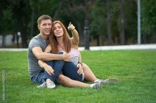 couple sitting on the grass in the park. Woman shows a finger gu © Himchenko