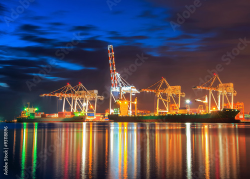 Container Cargo freight ship with working crane bridge in shipyard at dusk.