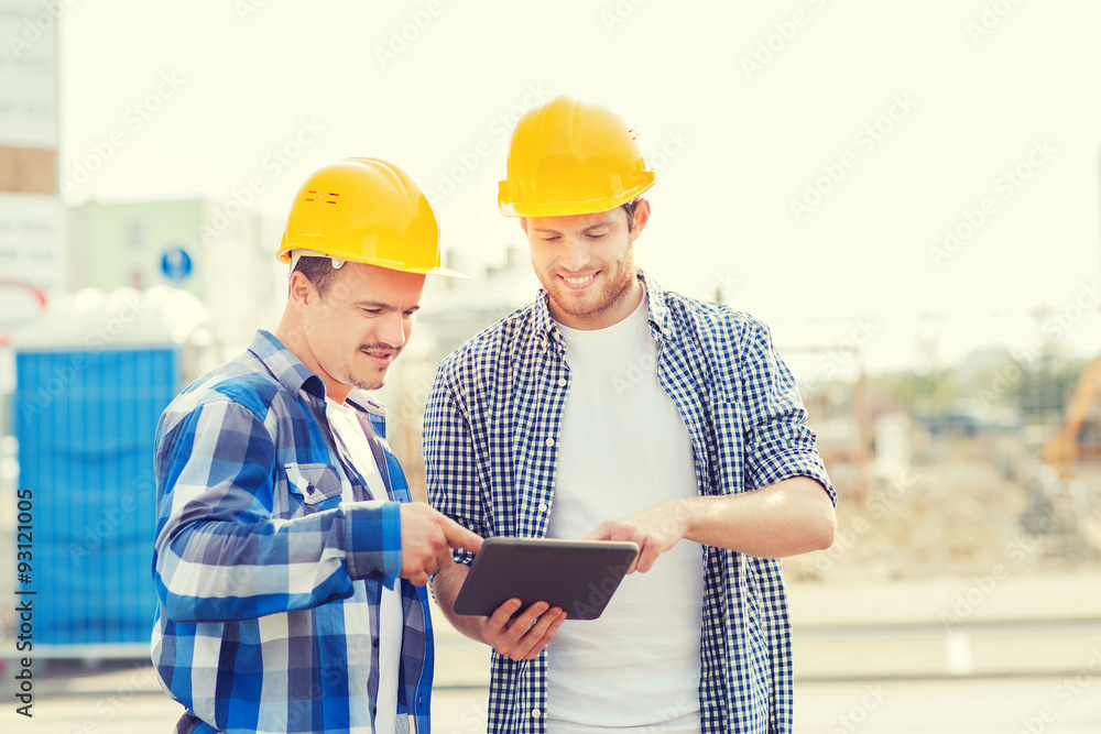 Fototapeta premium smiling builders in hardhats with tablet pc