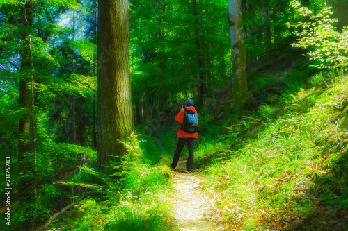 Man wearing red raincoat walking on a path in mountain forest taking a photo. Vintage effect.