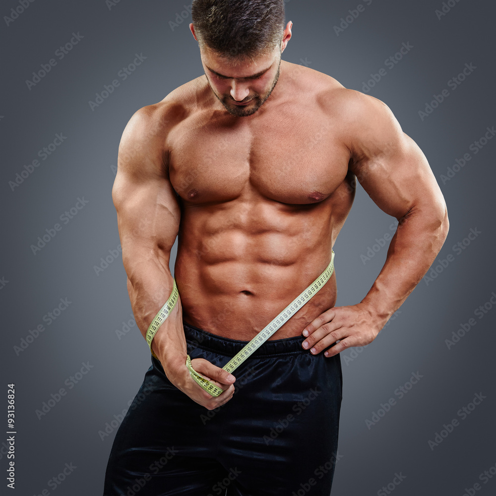 Muscular bodybuilder with perfect six pack abs looking down and holding  tape measure. Gain in abdominal muscles. Stock Photo