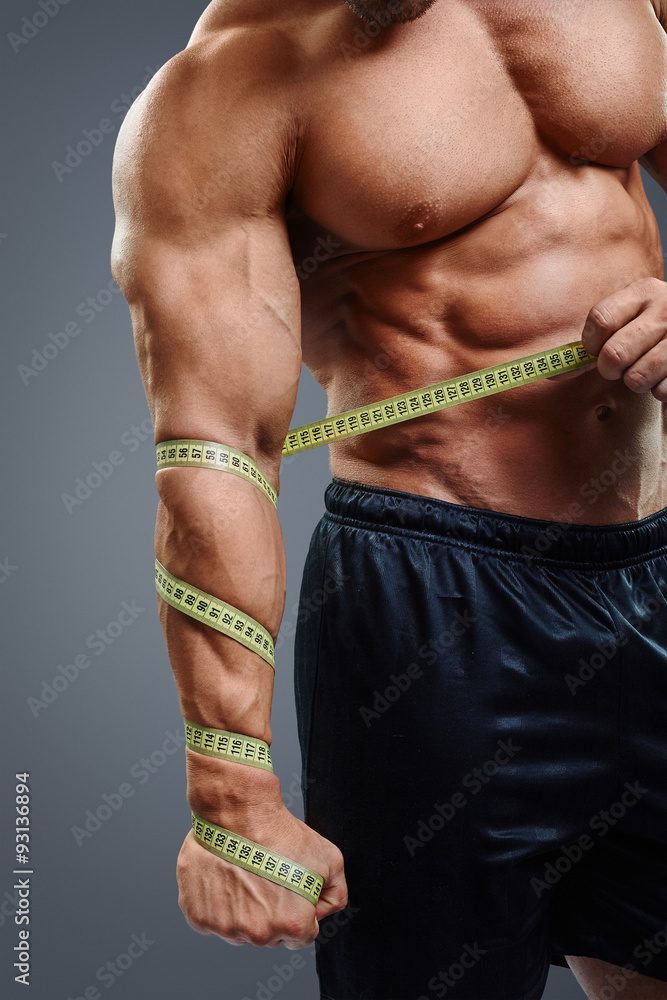 Closeup of bodybuilder holding tape measure. Cropped image of muscular arm  holding measuring tape isolated over gray background. Wrong muscle measuring.  Photos