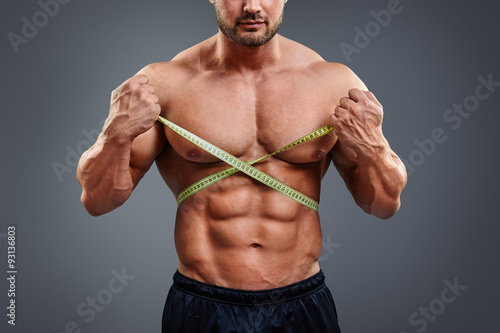Personal fitness trainer holding tape measure isolated over gray background. Closeup of muscular man measuring his waist. Doing perfect six pack abs.