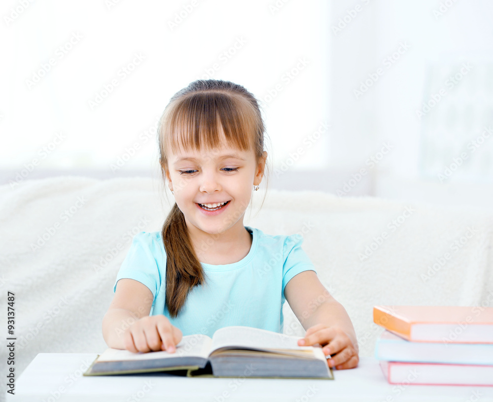 Beautiful little girl sitting on sofa with book, on home interior background Beautiful little girl sitting on sofa with book, on home interior background