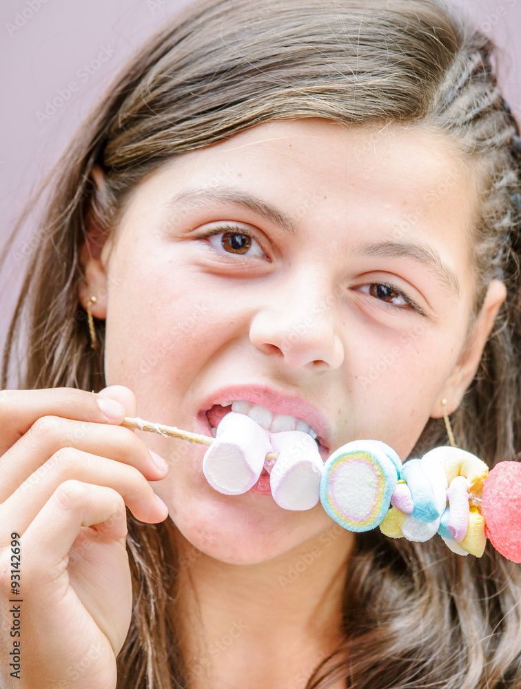 closeup of pretty young girl eating a delicious marshmallow skewer closeup of pretty young girl eating a delicious marshmallow skewer