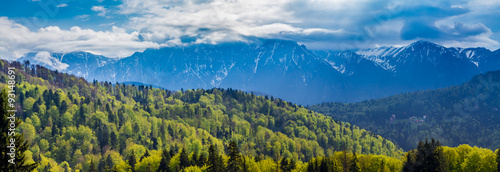 Romania, Predeal. Panorama with the snowy peaks of the Bucegi mountains and the green forests of Predeal,  in springtime, when the nature comes back to life and the snow starts to melt
