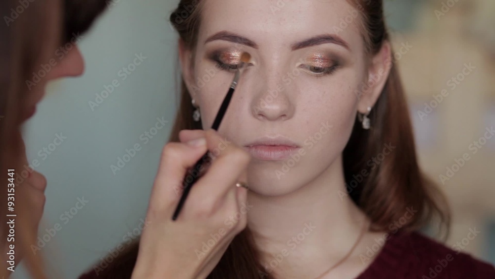 Makeup artist doing a gorgeous evening smokey eyes on young beautiful redhead woman Makeup artist doing a gorgeous evening smokey eyes on young beautiful redhead woman
