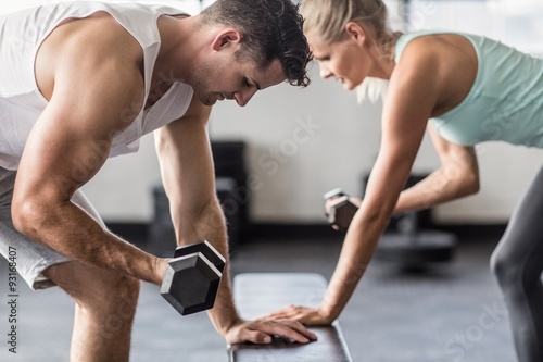 couple exercising with dumbells on a workout bench