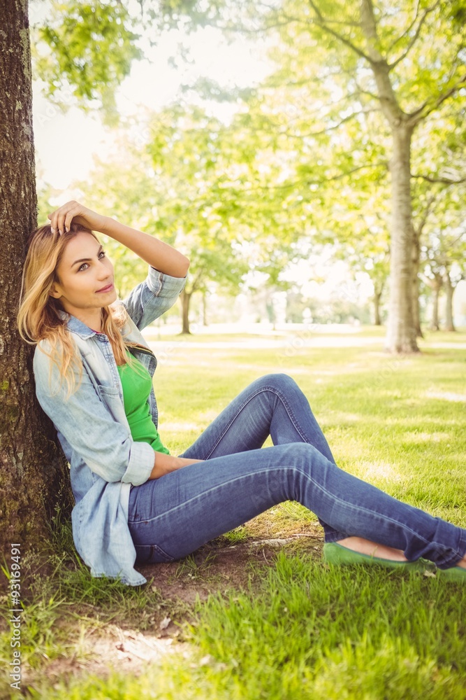 Smiling woman with hand in hair while sitting under tree Smiling woman with hand in hair while sitting under tree