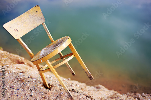 unstable precarious position. chair on the edge of the crumbling high sandy shore, the concept of precariousness
