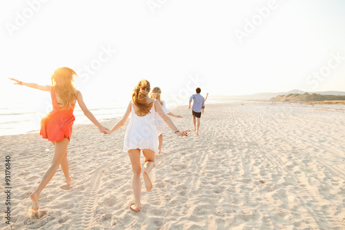 A group of friends runs on the deserted beach at sunset in the direction of the sunset. The last hours of day on the beach to have fun during the summer a group of teenagers. Two friends holding hands