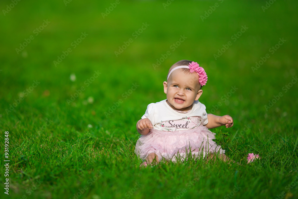 A little baby in a pink clothes sits on a grass