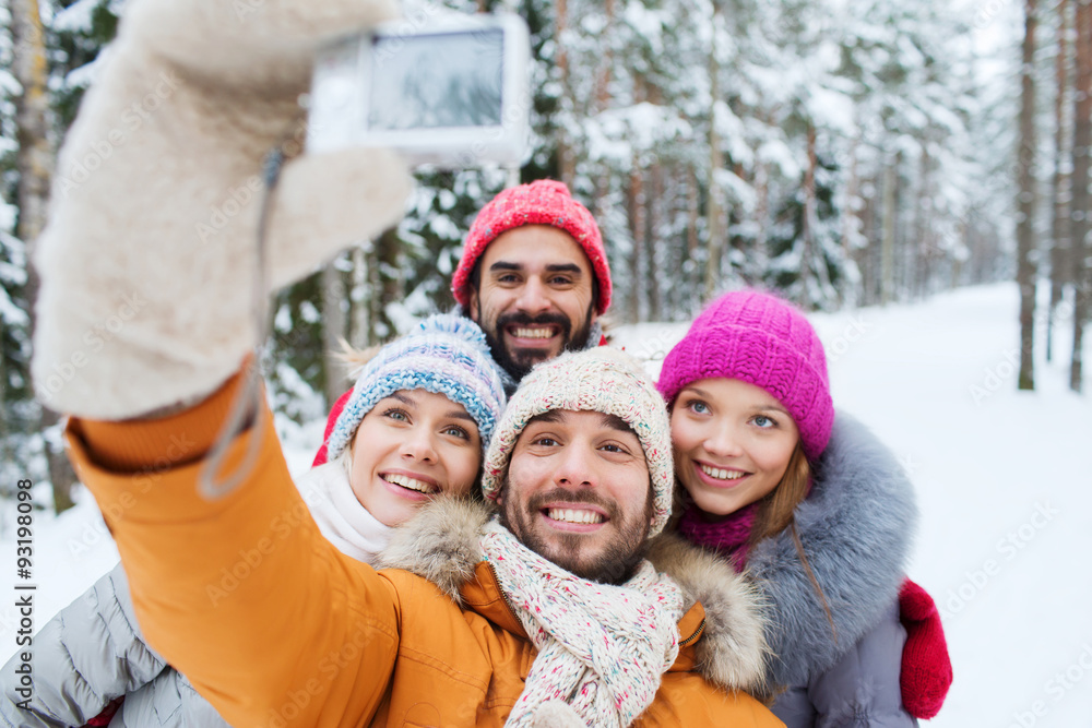 smiling friends with camera in winter forest