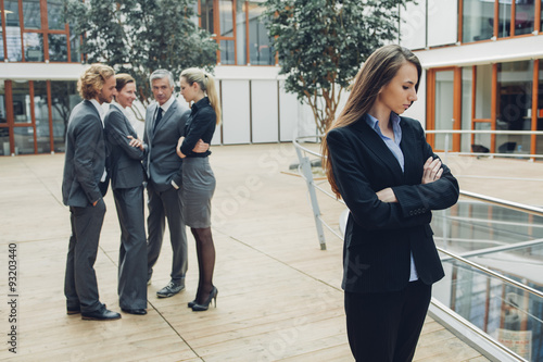 Businesswoman with crossed arms, excluded from group of business people