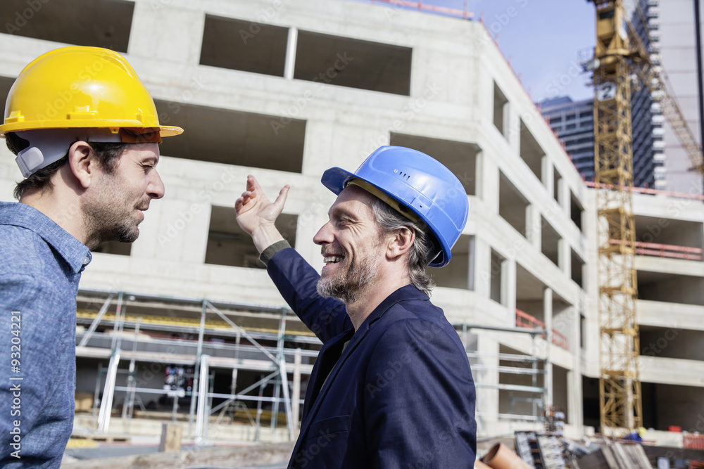 Two men on construction site wearing hard hats Two men on construction site wearing hard hats