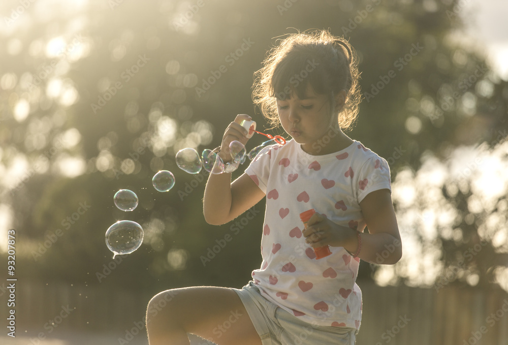 Little girl making soap bubbles in the park at twilight Little girl making soap bubbles in the park at twilight