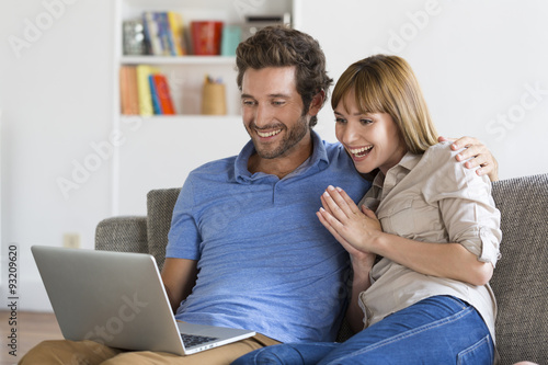 Happy successful young couple with laptop on sofa in modern apartment