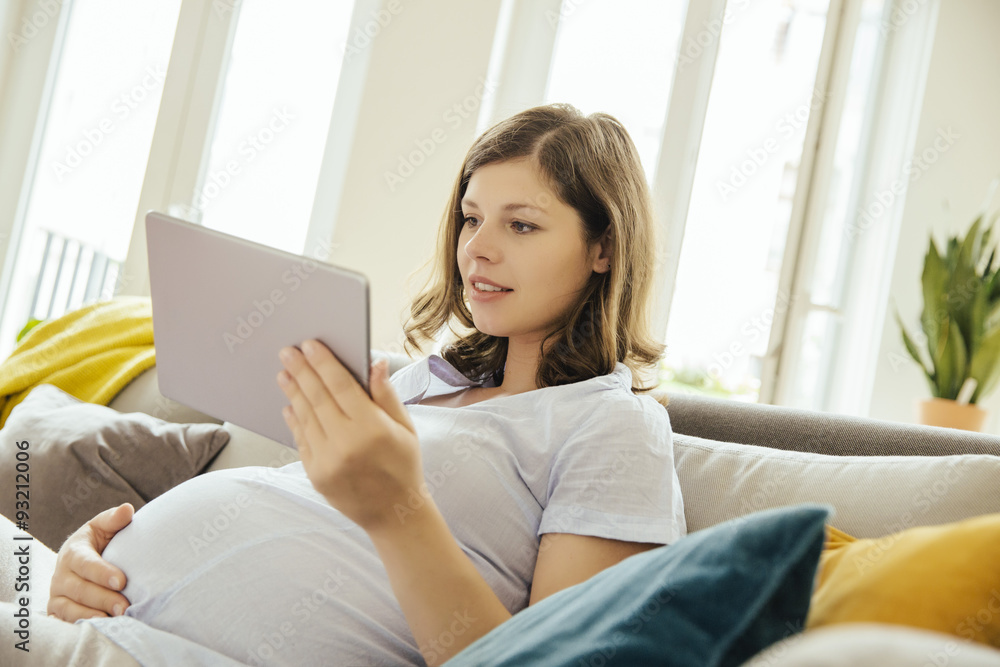Pregnant woman with digital tablet relaxing on couch at home Pregnant woman with digital tablet relaxing on couch at home