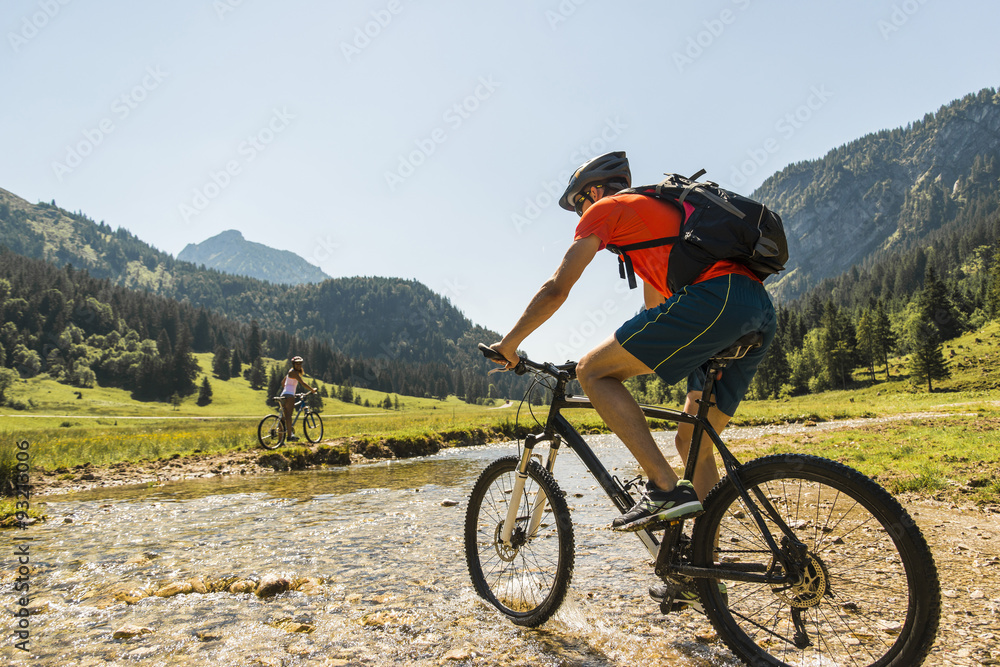 Austria, Tyrol, Tannheim Valley, young man on mountain bike crossing brook Austria, Tyrol, Tannheim Valley, young man on mountain bike crossing brook