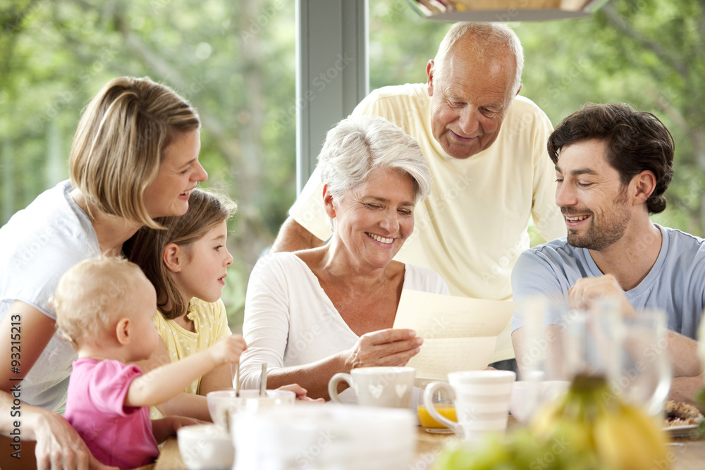 Happy granddaughter with her family reading letter at breakfast table Happy granddaughter with her family reading letter at breakfast table