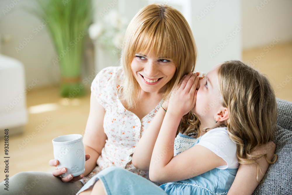 Mother and daughter sitting on couch with drinking cups Mother and daughter sitting on couch with drinking cups