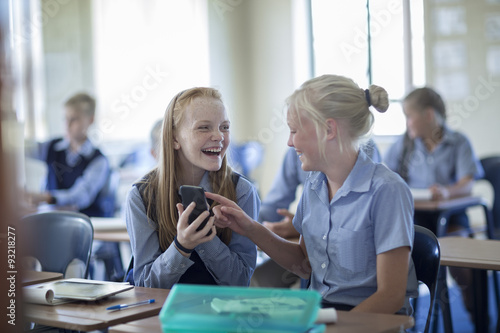 Two happy schoolgirls in classroom with cell phone photo