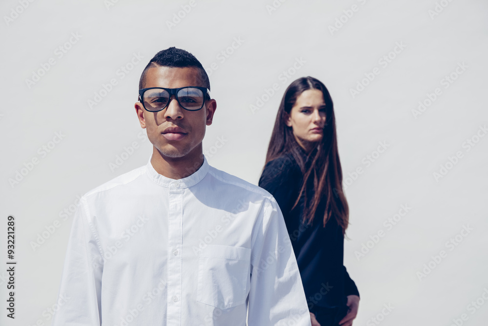 Portrait of young man with glasses and woman behind him standing in front of white background Portrait of young man with glasses and woman behind him standing in front of white background