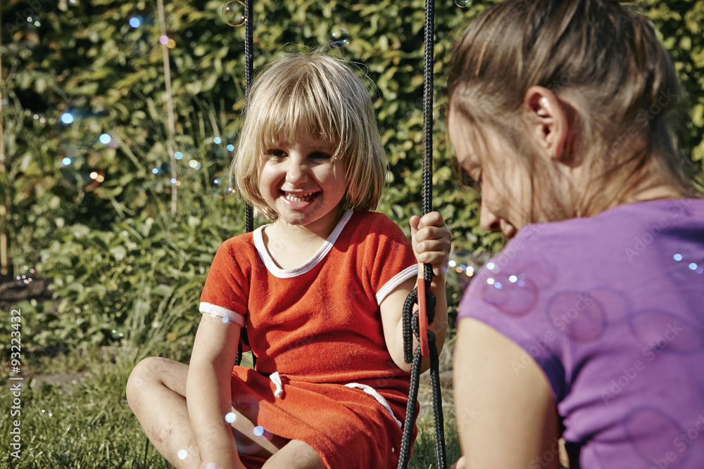 Mother and daughter on swing surrounded by soap bubbles Mother and daughter on swing surrounded by soap bubbles