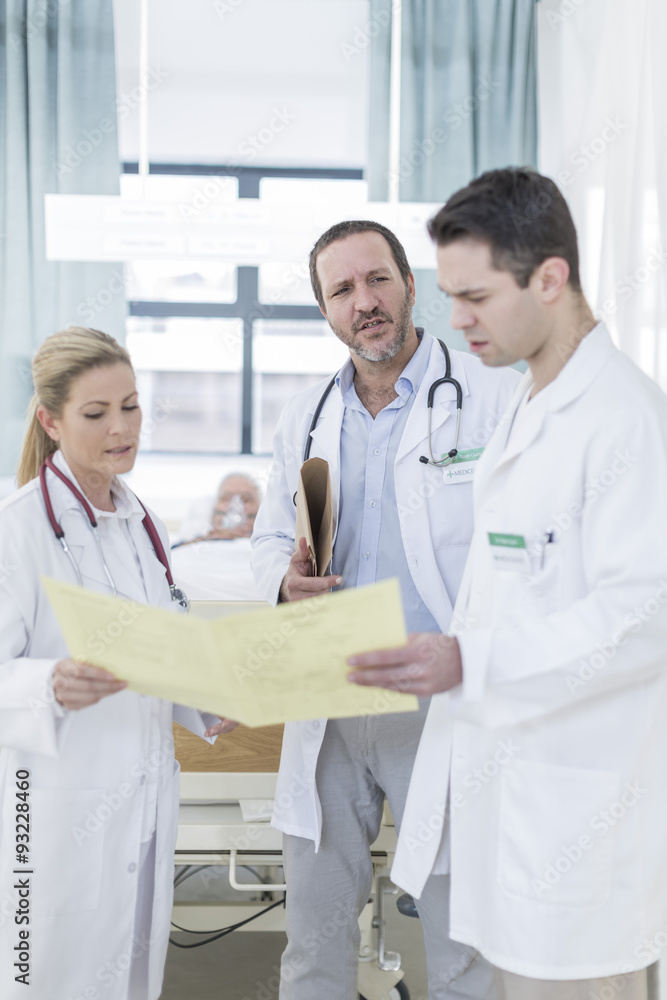 Three doctors with report in a hospital room Three doctors with report in a hospital room