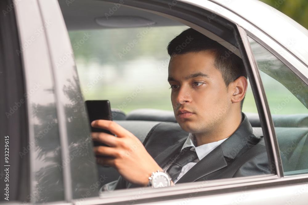 Young businessman using phone while traveling to work by car