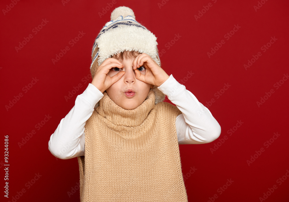 girl in hat and sweater look through binoculars on red background