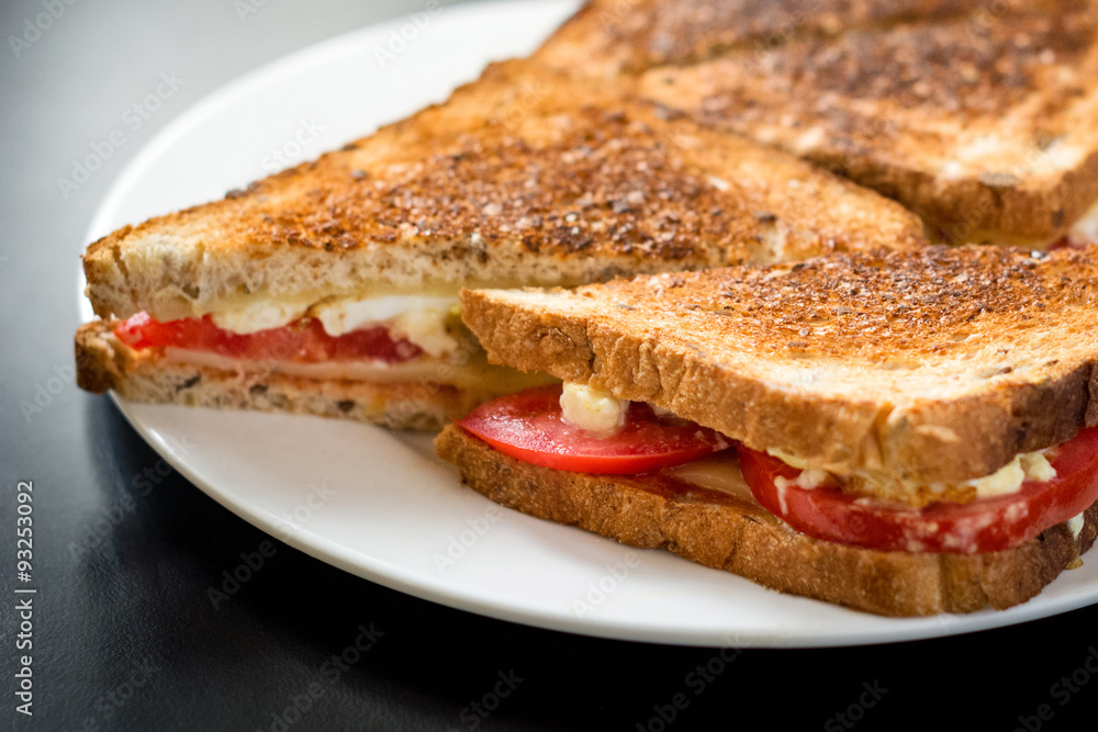 Toasted ham and cheese sandwich on white plate on black background Toasted ham and cheese sandwich on white plate on black background