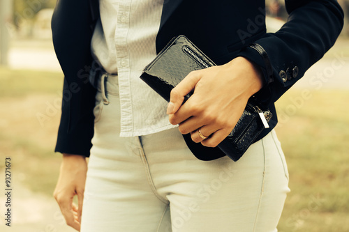 Woman in jeans, shirt and a black jacket holding a purse in her