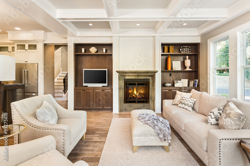 Beautiful living room interior with hardwood floors, coffered ceiling, and roaring fire in fireplace in new luxury home
