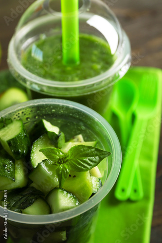 Green vegetable and fruit salad and healthy fresh drink in plastic cups on wooden background. Colorful diet concept