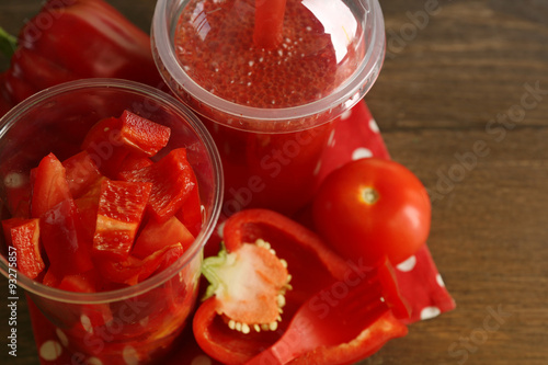 Red vegetable and fruit salad and healthy fresh drink in plastic cups on wooden background. Colorful diet concept