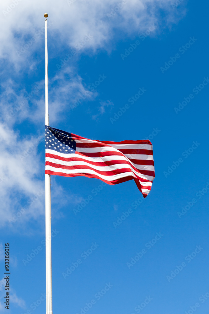 Fototapeta premium American flag flying at half mast against blue sky with white clouds. Copy space