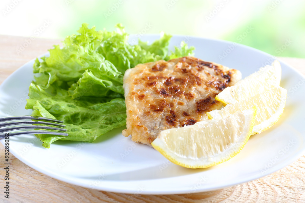 Dish of fish fillet with lettuce and lemon on table close up Dish of fish fillet with lettuce and lemon on table close up