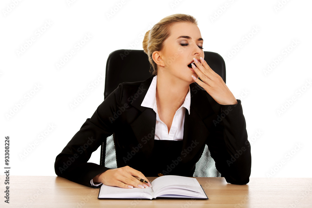 Yawning businesswoman writing note by a desk Yawning businesswoman writing note by a desk