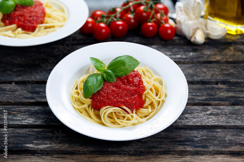 Spaghetti with marinara sauce and basil leaves on top, decorated with vegetables, olive oil. on wooden table.