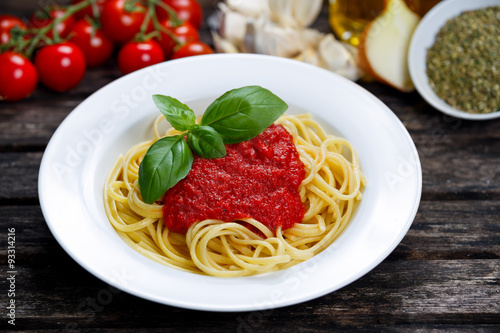 Spaghetti with marinara sauce and basil leaves on top, decorated with vegetables, olive oil, italian herbs. on wooden table.
