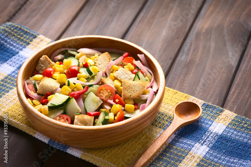 Fresh vegetable salad of sweet corn, cherry tomato, cucumber, red onion, red pepper, chives with croutons, photographed with natural light (Selective Focus, Focus one third into salad)