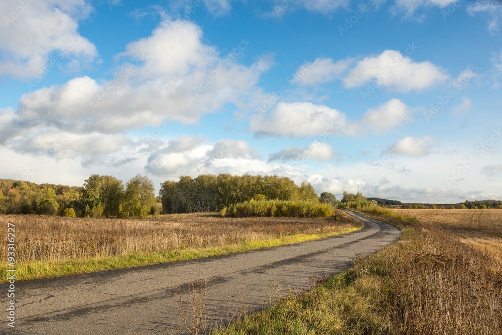 country road and cumulus clouds over the retracted fields